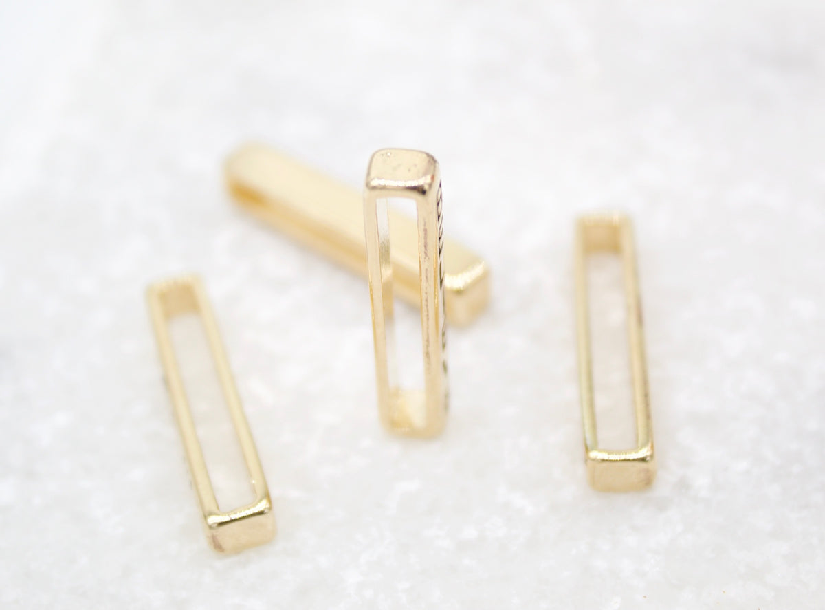 Four shiny gold rectangular slider beads rest on a white surface.