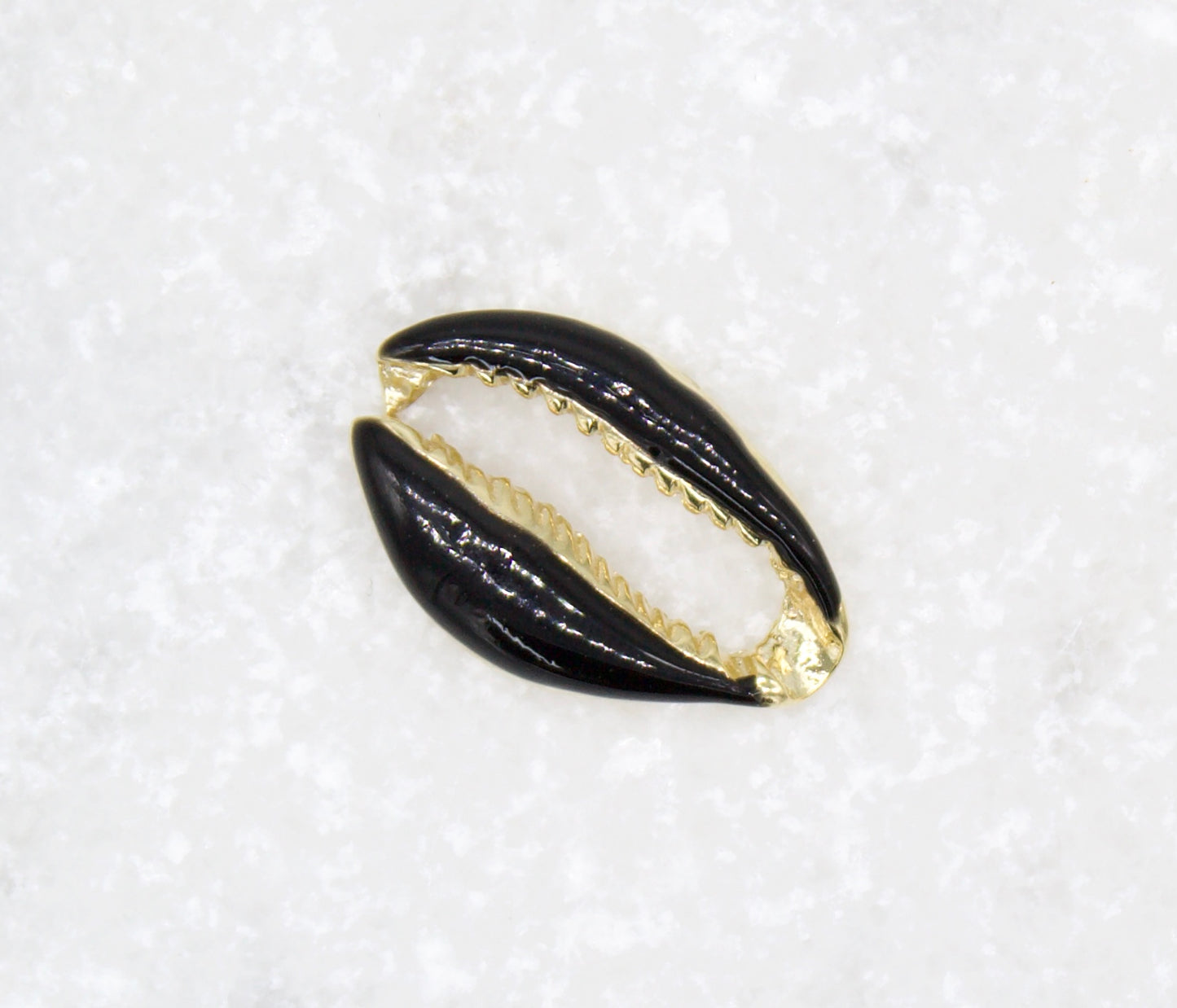 A glossy black and gold cowrie shell pendant rests on a textured white surface.