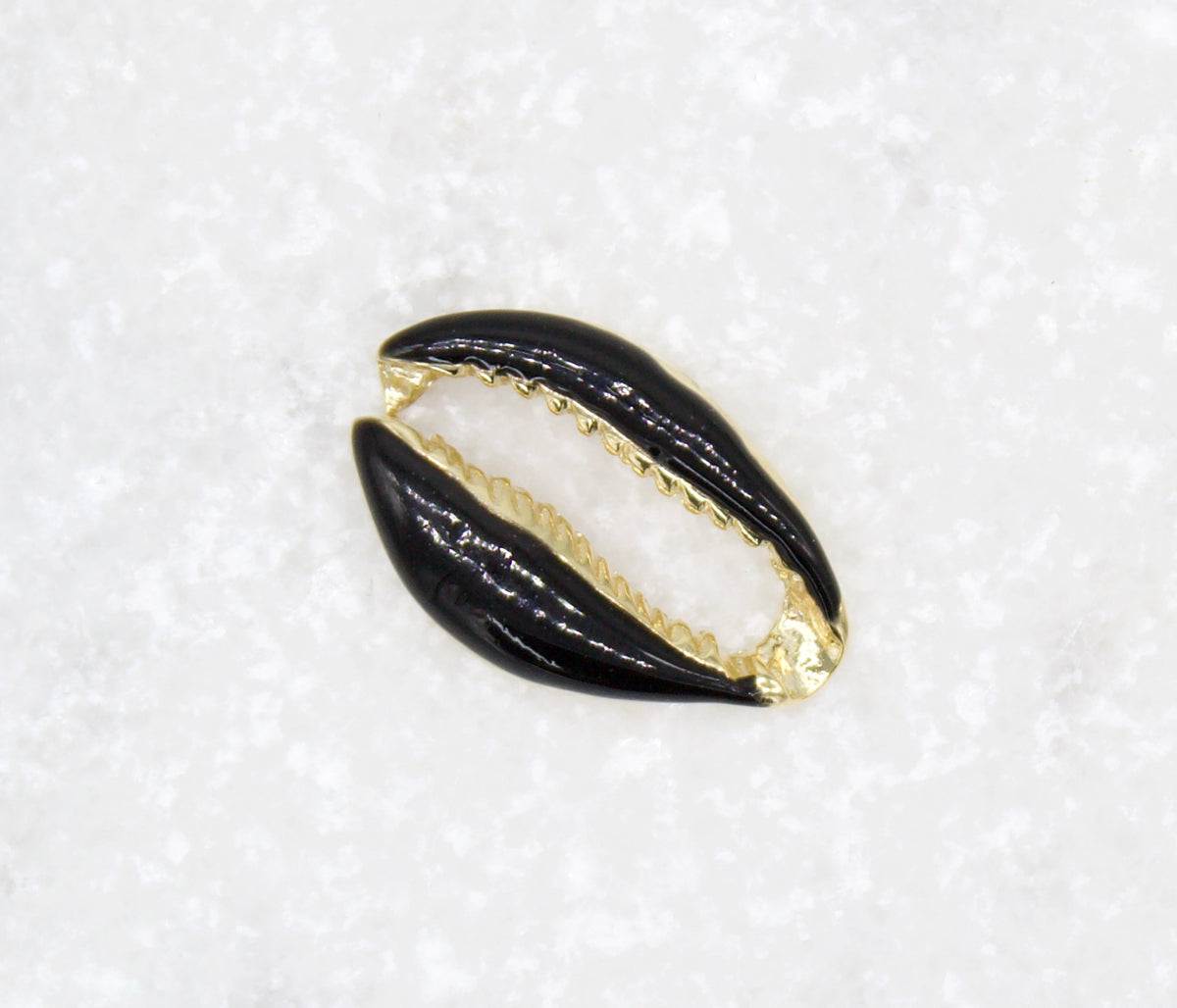 A glossy black and gold cowrie shell pendant rests on a textured white surface.