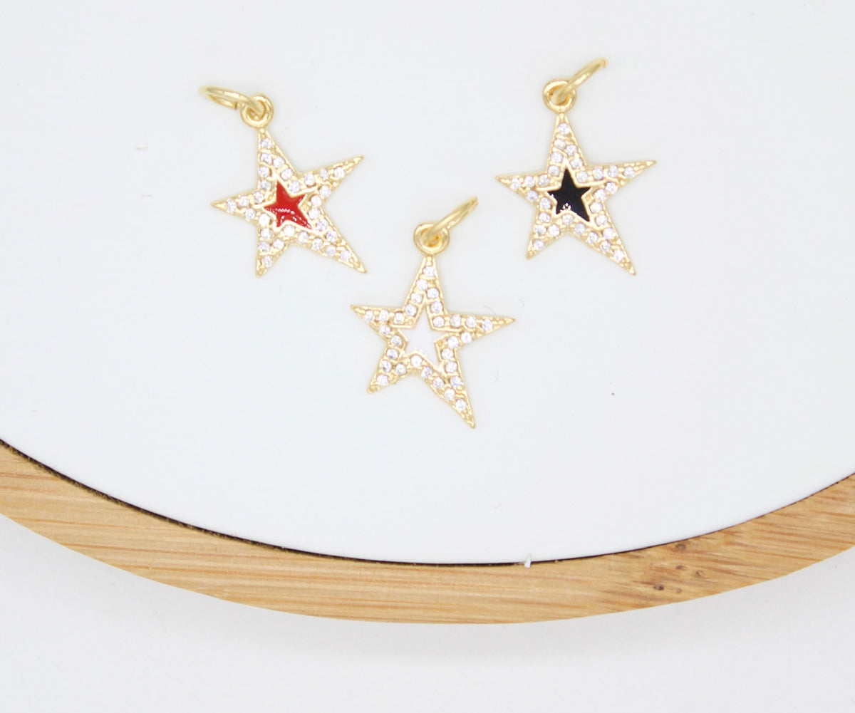 Three gold star charms paved with sparkling cubic zirconia rest on a white surface, featuring red, black, and open-center details.