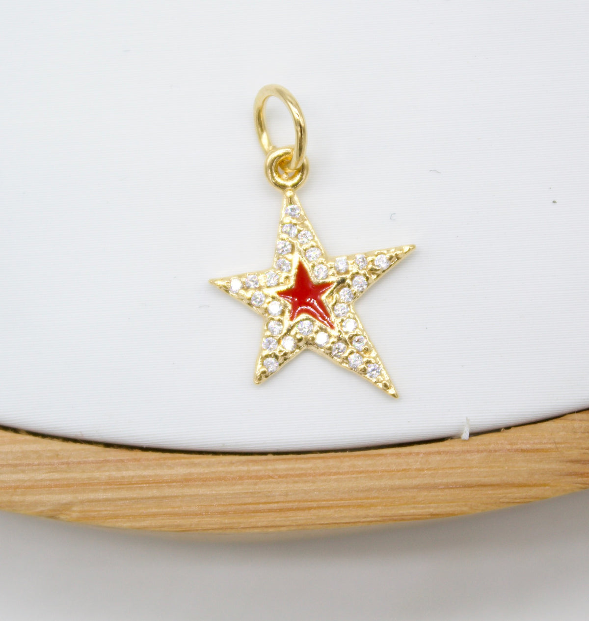 A gold star pendant sparkles with tiny pave diamonds and features a vibrant red enamel center against a white background.