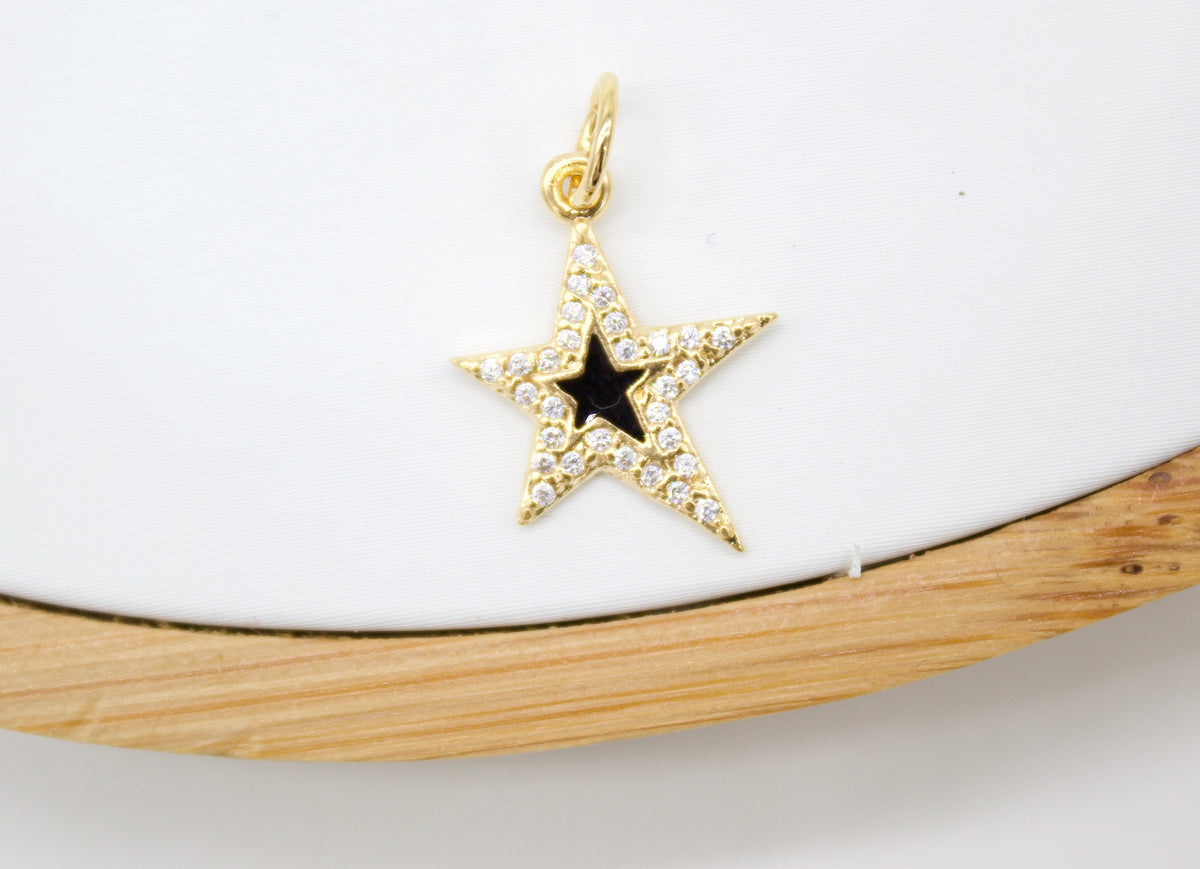 A sparkling gold star pendant features a central black enamel star studded with pave diamonds resting on a neutral white surface.