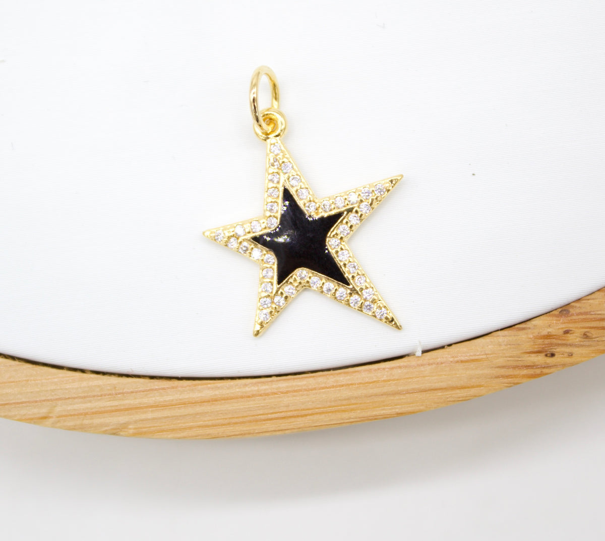 A gold star pendant with a black enamel center and sparkling cubic zirconia pavé rests on a white display against a wooden background.