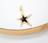 A gold star pendant with a black enamel center and sparkling cubic zirconia pavé rests on a white display against a wooden background.
