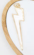 A white enamel and gold-trimmed lightning bolt pendant rests on a white display surface with a wooden rim.