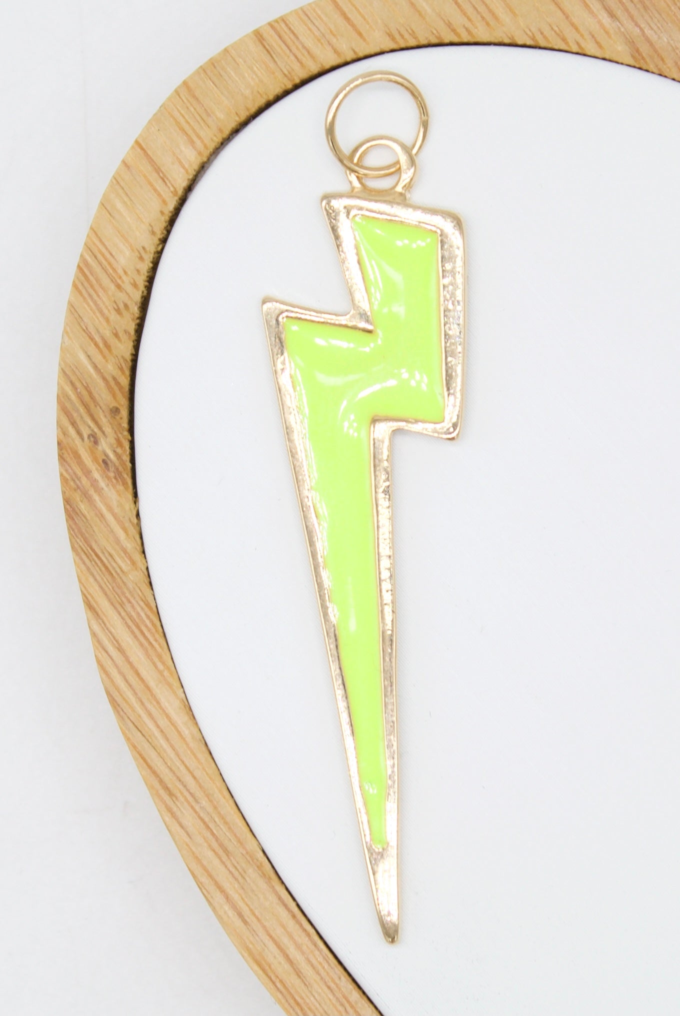A bright neon green enamel lightning bolt pendant rests inside a round wooden display tray.
