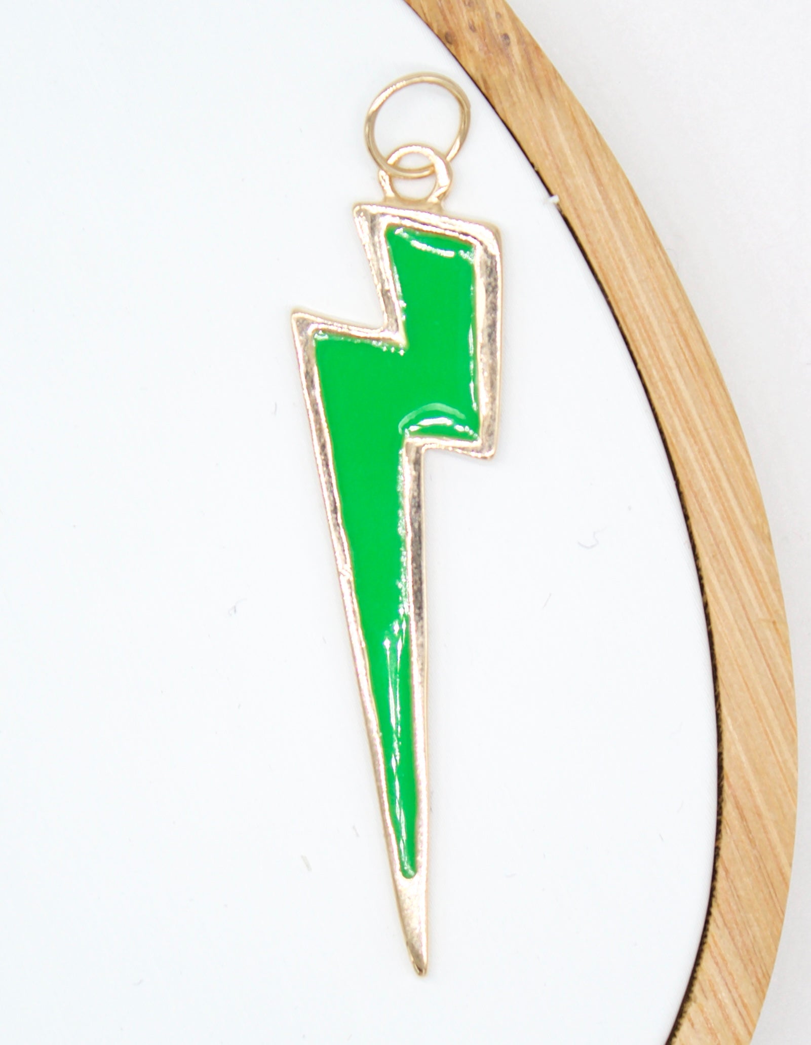 A bright green enamel lightning bolt charm hangs vertically inside a wooden embroidery hoop.