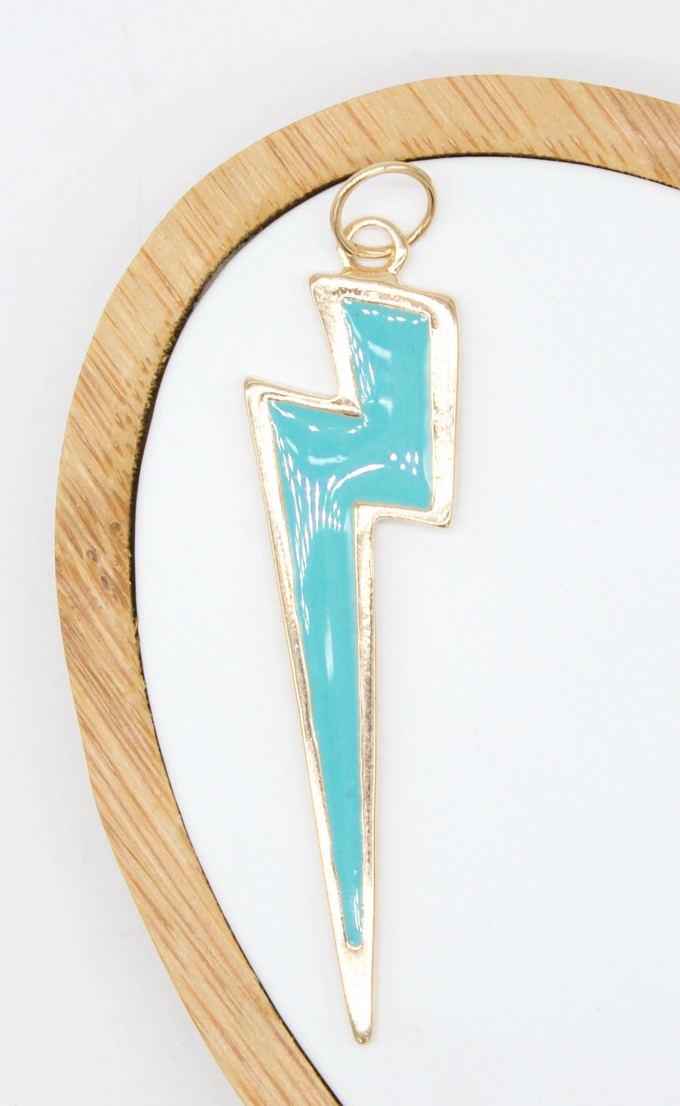 A gold and turquoise enamel lightning bolt charm rests on a white background inside a wooden display ring.