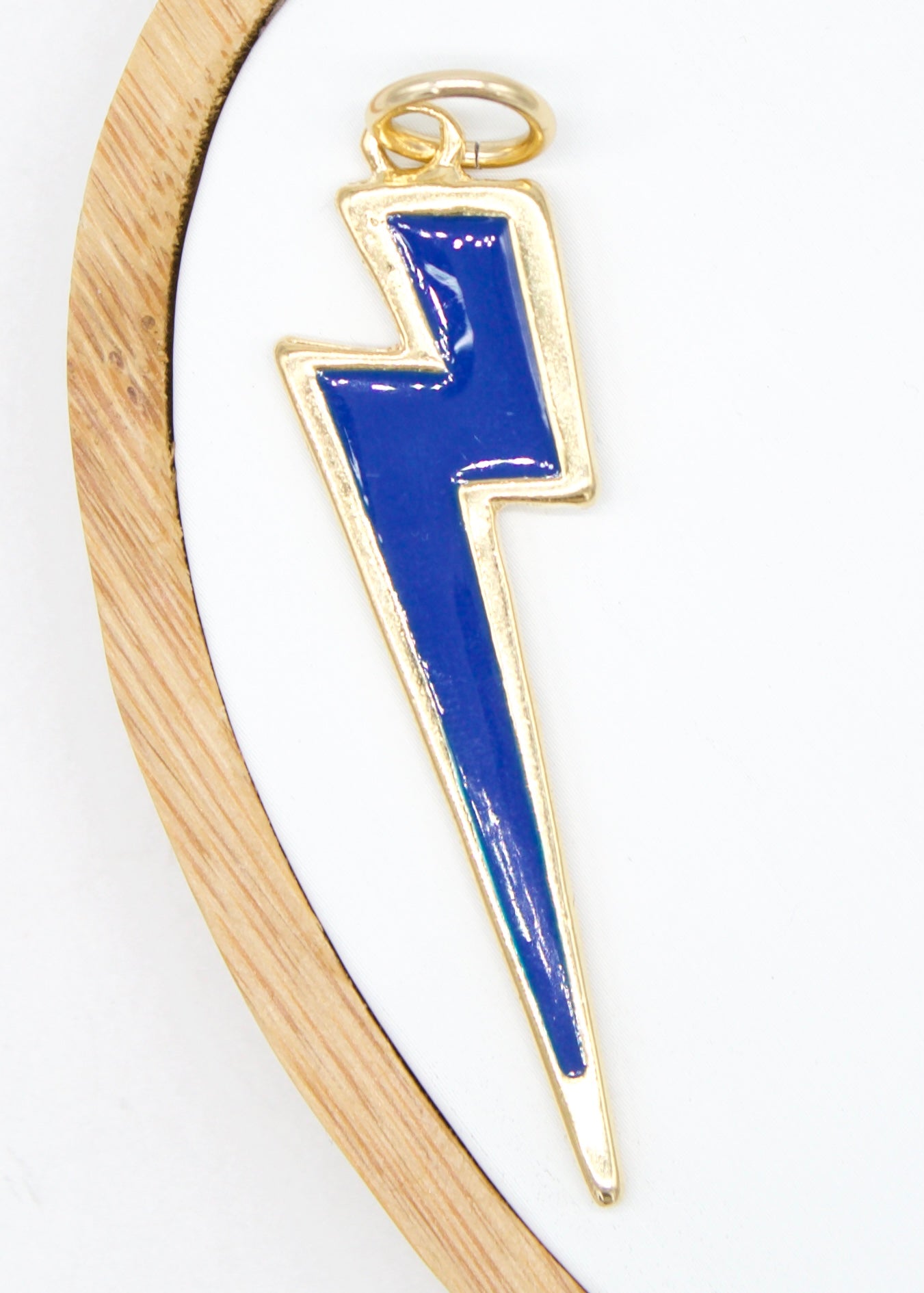 A blue and gold enamel lightning bolt charm rests inside a wooden display hoop.