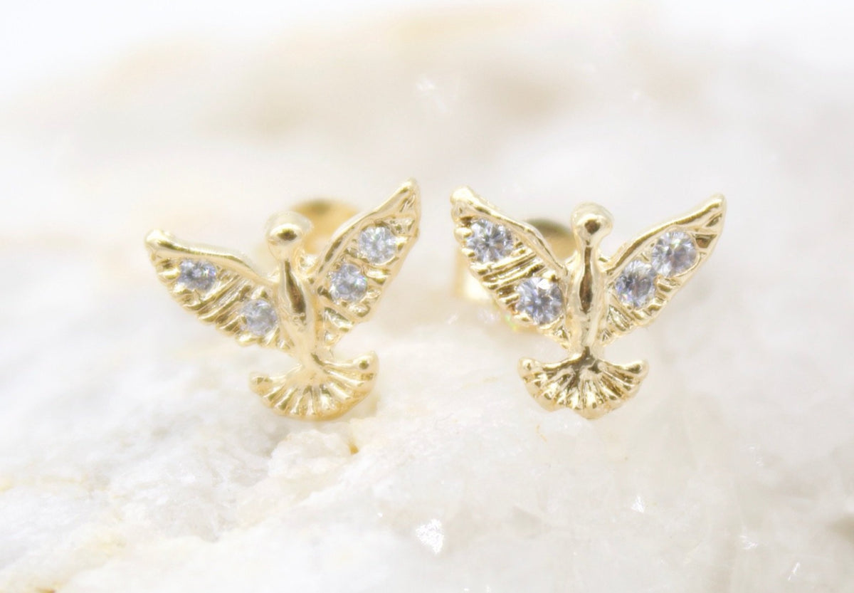 A pair of gold dove earrings with sparkling cubic zirconia stones rest on a light background.