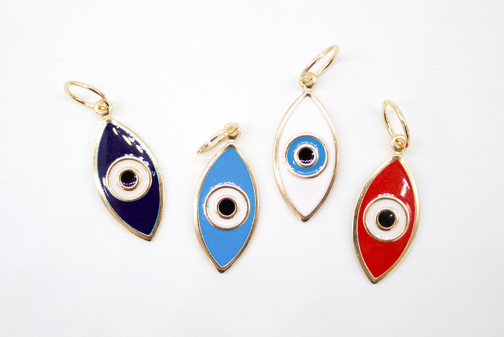 Four colorful evil eye charms in navy blue, light blue, white, and red enamel with gold frames lie on a white surface.