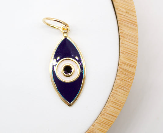 A gold evil eye pendant with dark blue and white enamel rests on a white display surface next to a wooden ring.