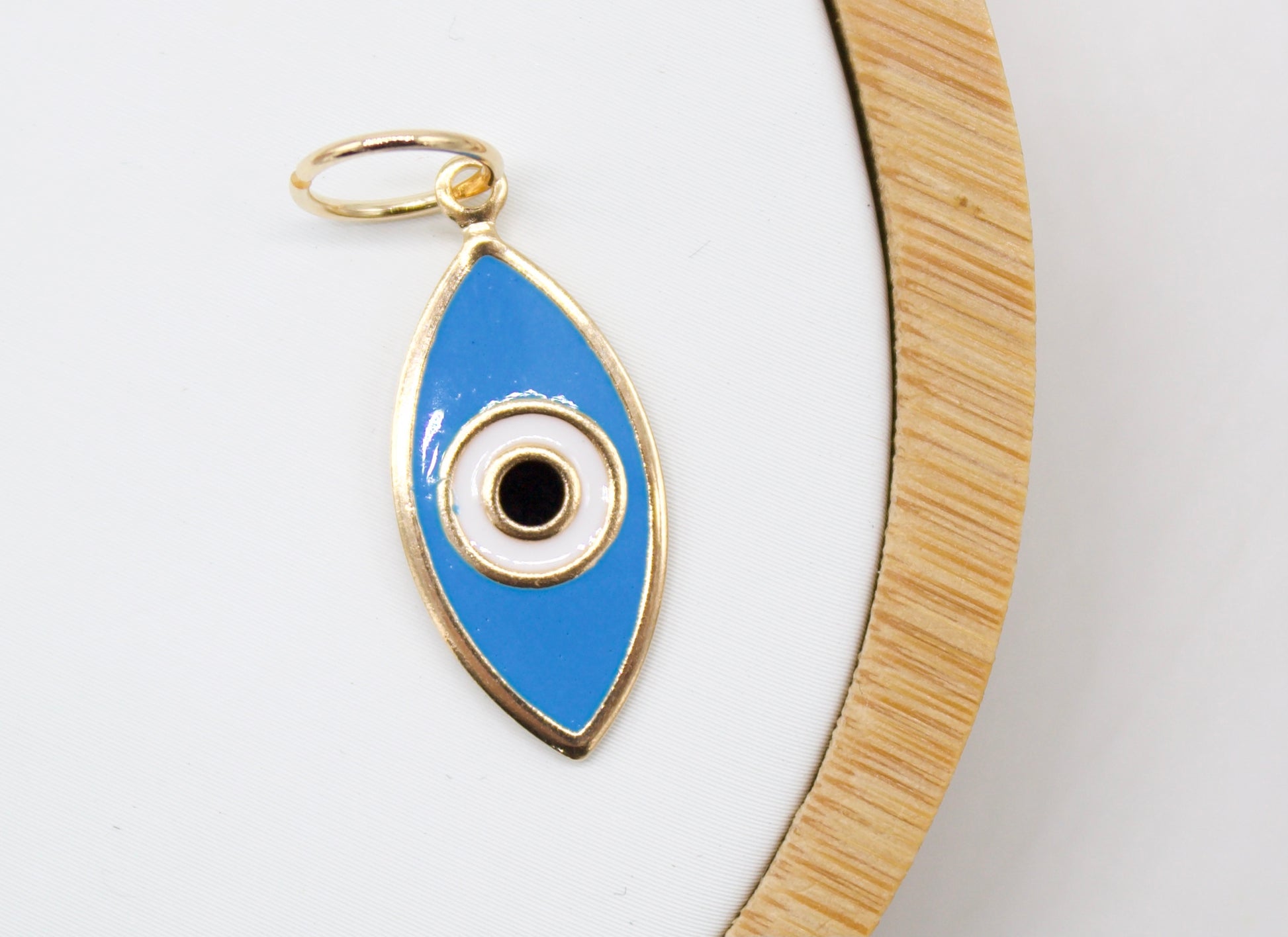 A gold-rimmed evil eye charm featuring blue and white enamel rests on a white display surface.