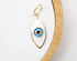 A delicate gold evil eye charm featuring white enamel and blue concentric circles rests on a neutral white display tray.