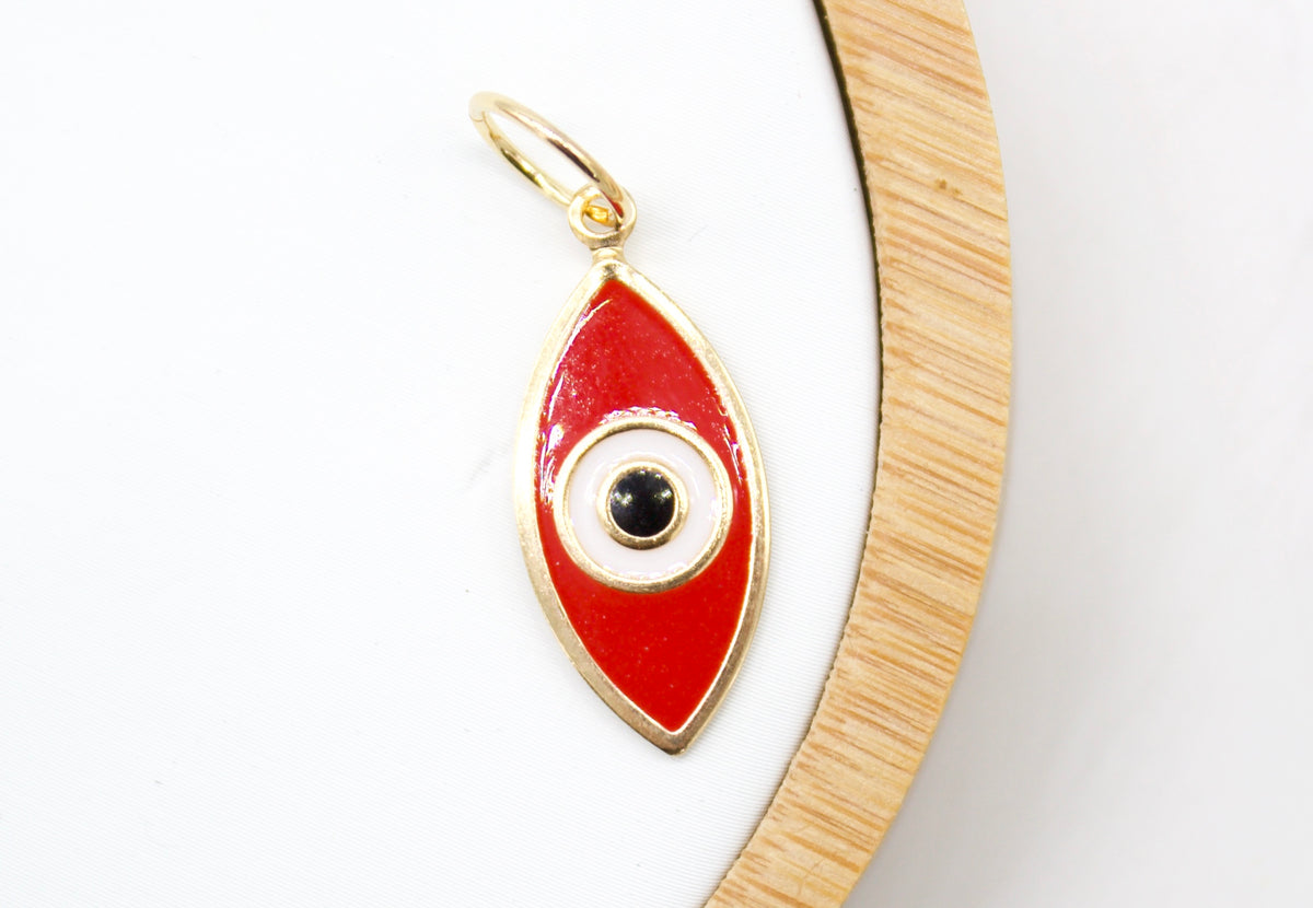 A gold evil eye pendant featuring red enamel rests on a white and wooden display surface.