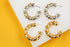 Two pairs of metallic spiral hoop earrings, one in silver and one in gold, rest on a white and yellow display background.