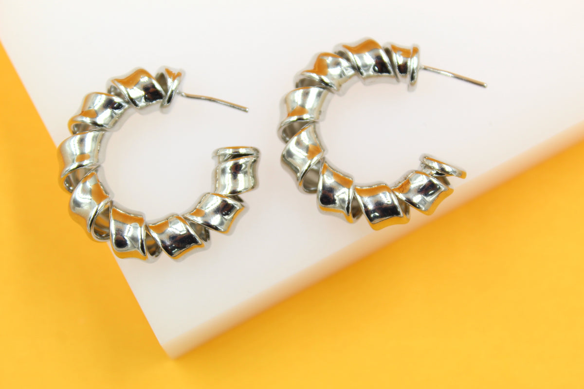 A pair of shiny silver spiral hoop earrings rests on a white and yellow background.