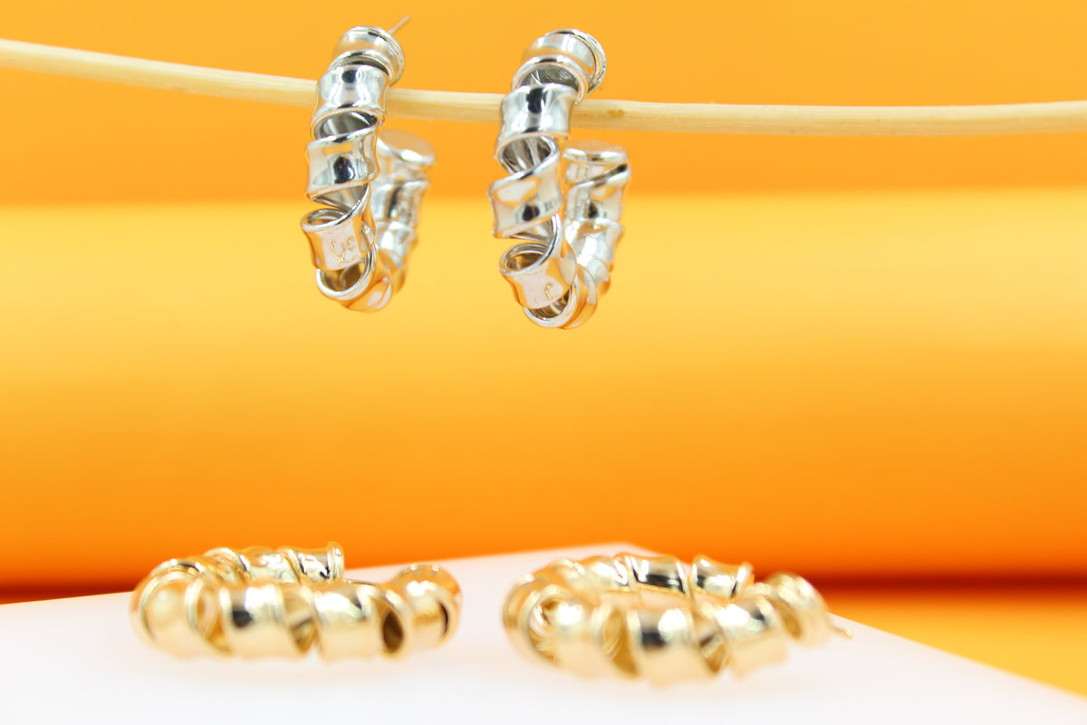 Two pairs of shiny silver and gold spiral hoop earrings rest against a vibrant orange and white background.