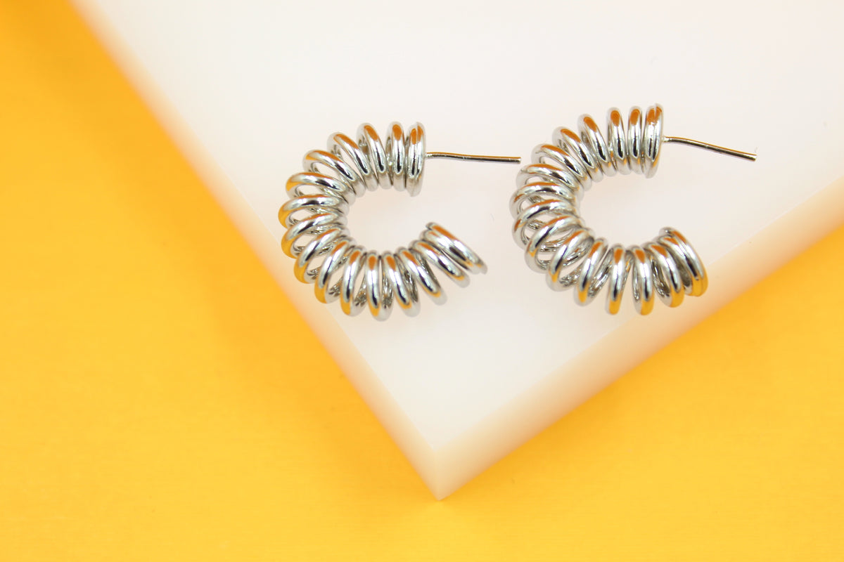 A pair of silver chunky spiral hoop earrings rests on a white and yellow display stand.