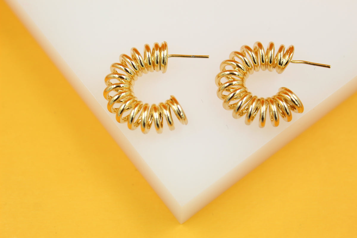A pair of shiny gold spiral hoop earrings rests on a white and yellow display stand.