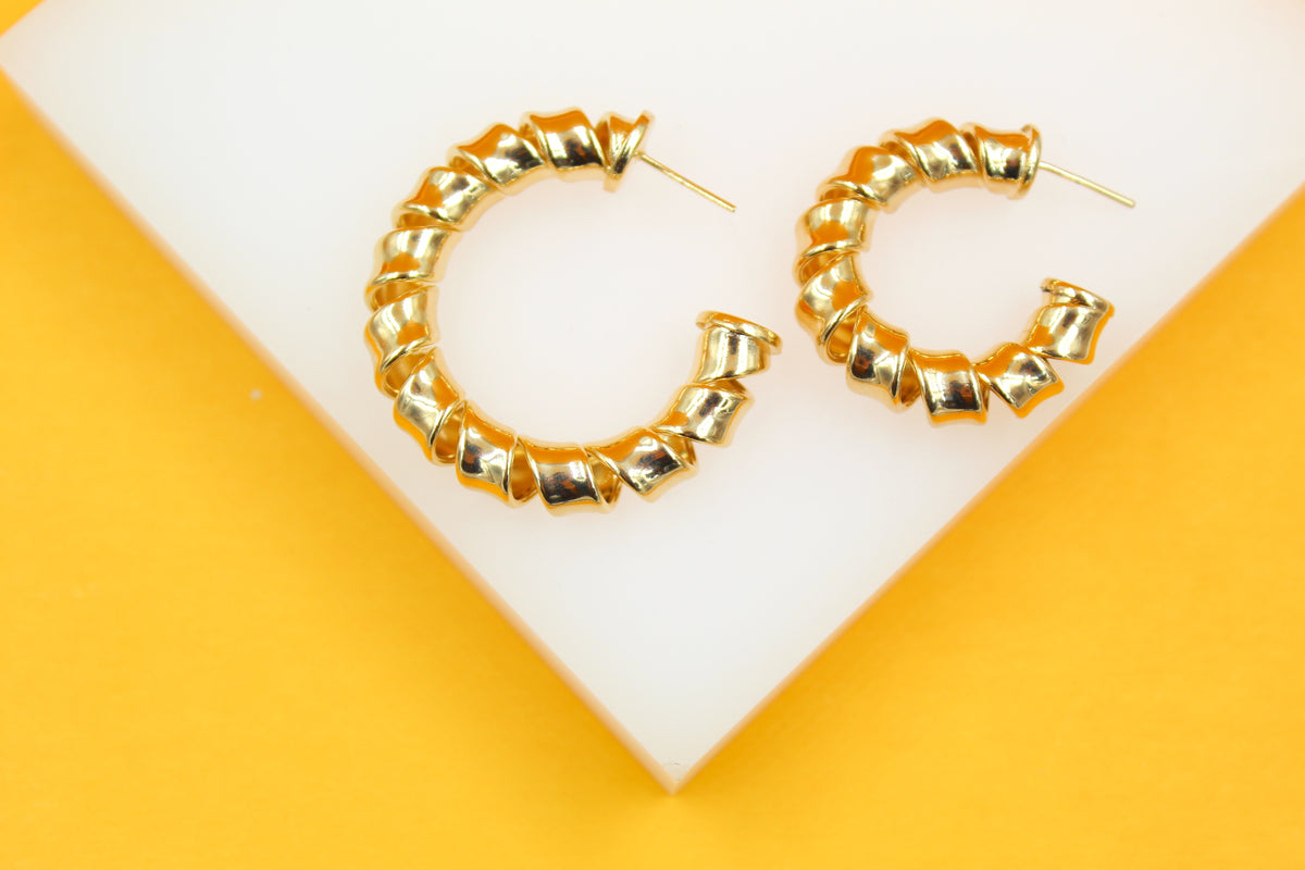 A pair of gold spiral hoop earrings rests on a white and yellow display stand.