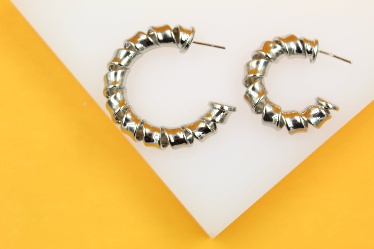 Two chunky silver spiral hoop earrings rest on a white and yellow background.