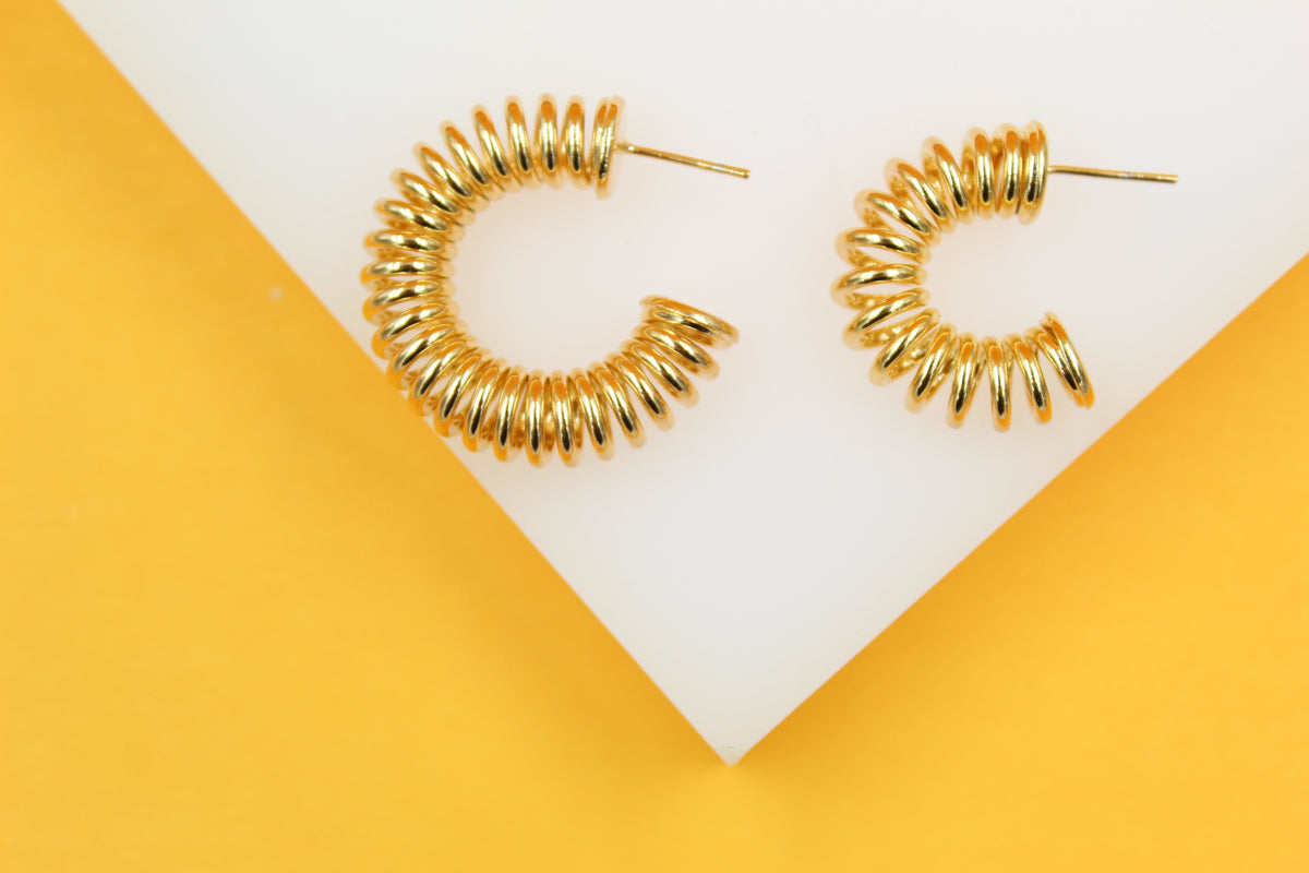 A pair of shiny gold spiral hoop earrings rests on a white and yellow geometric display block.