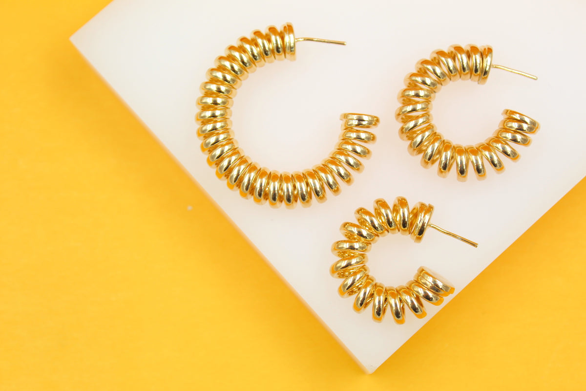Three thick gold hoop earrings rest on a white display against a vibrant yellow background.
