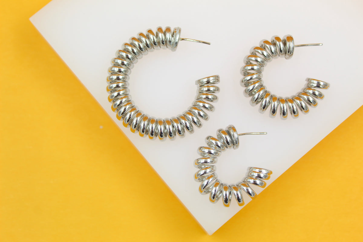 Three silver spiral hoop earrings display a unique coiled design on a white and yellow background.