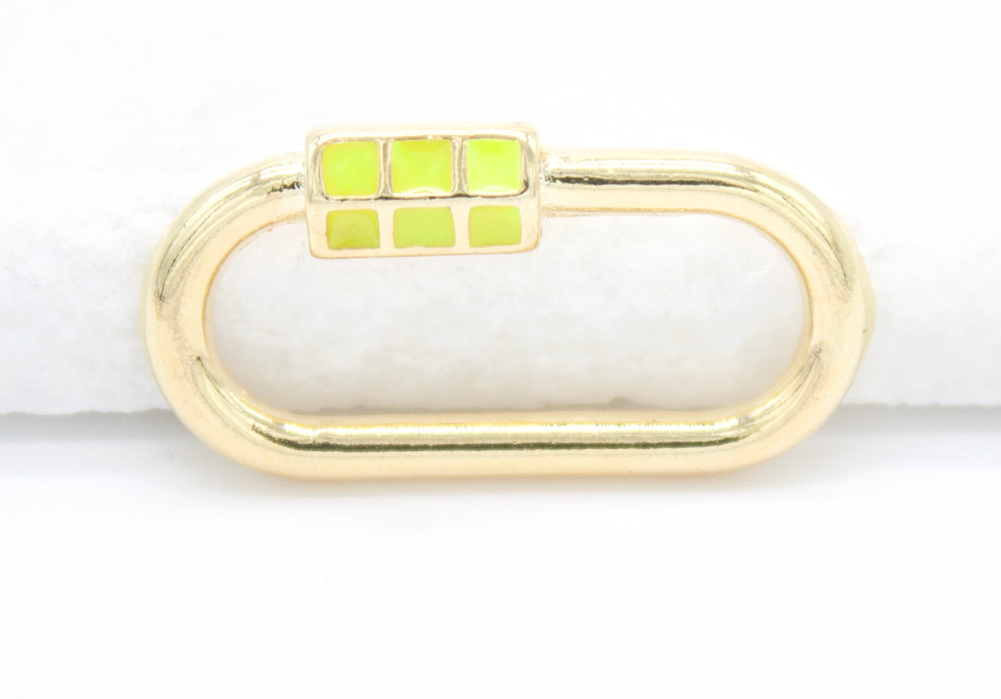 A gold oval charm with a neon yellow enamel block accent rests against a plain white background.