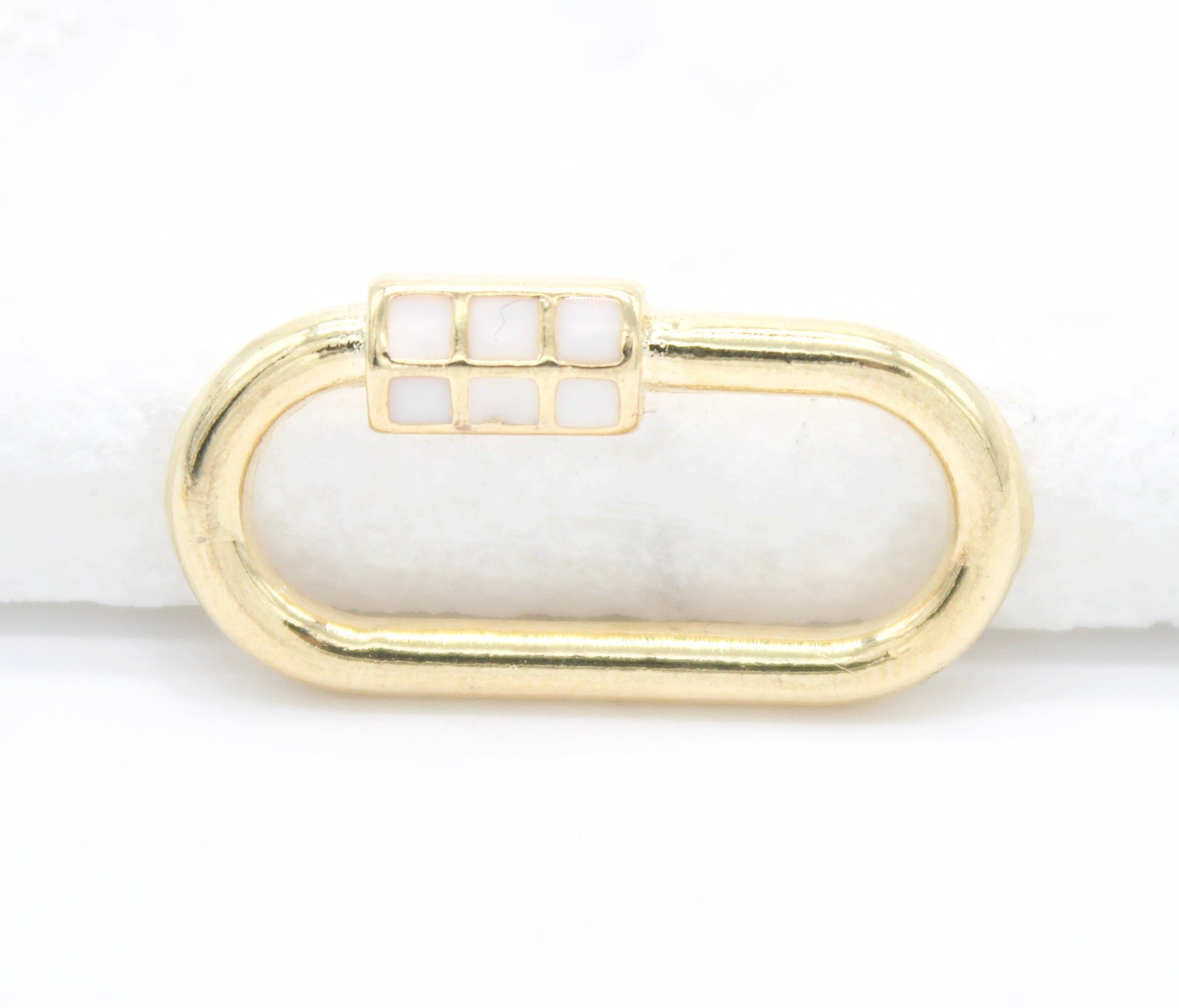 A gold oval charm connector features a white enamel grid clasp on a white background.