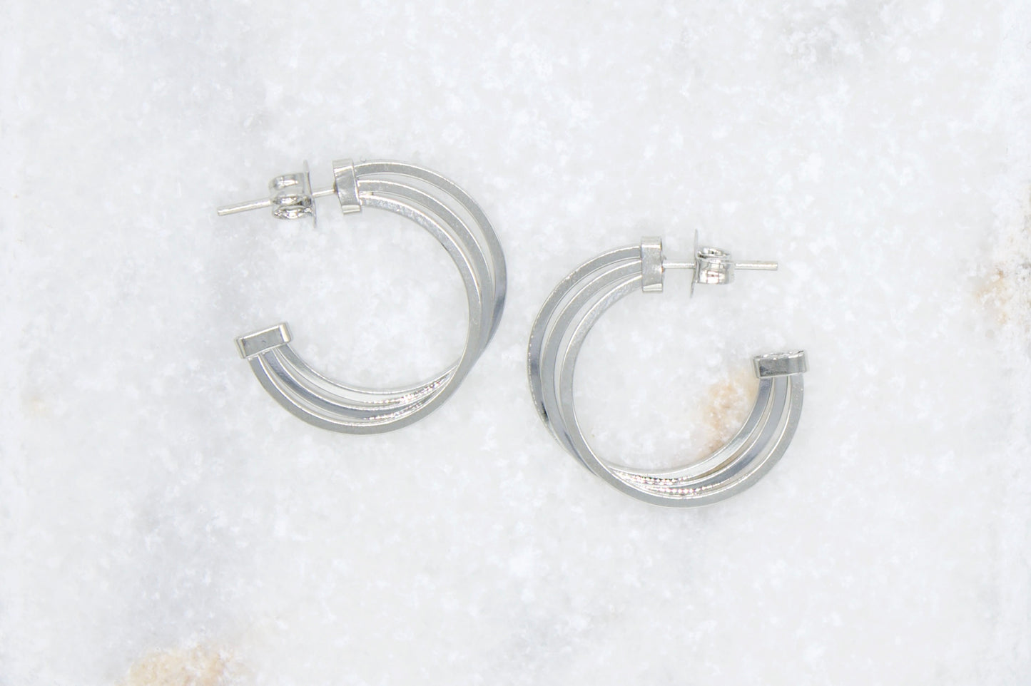 A pair of triple-band silver hoop earrings rests on a white marble surface.
