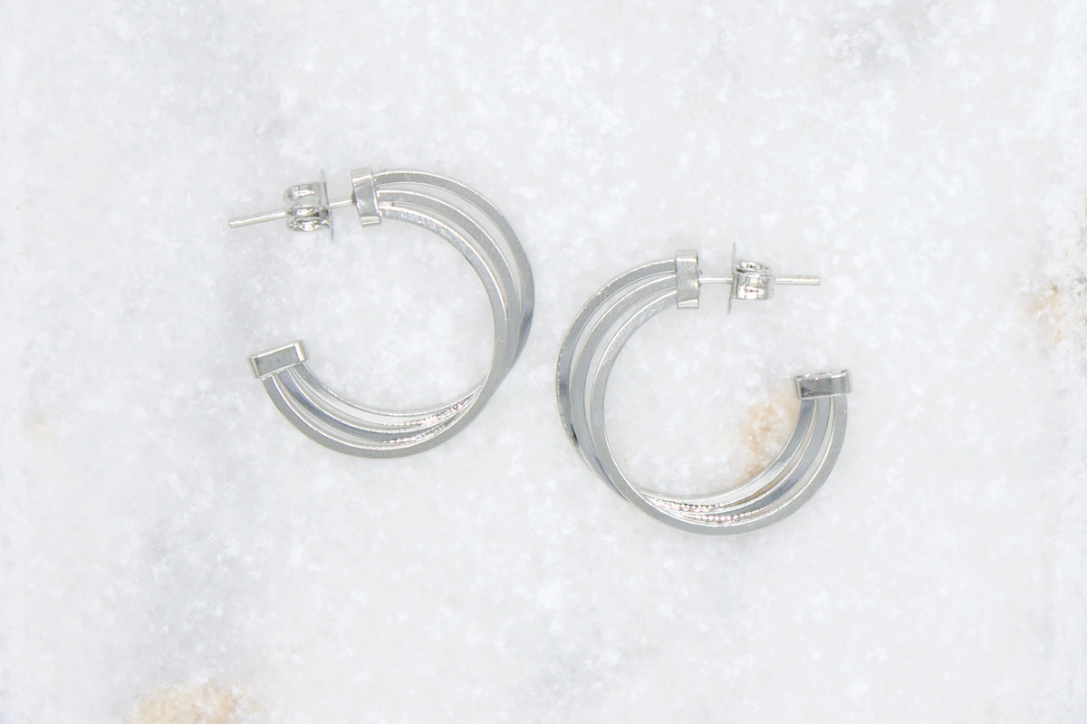 A pair of triple-band silver hoop earrings rests on a white marble surface.