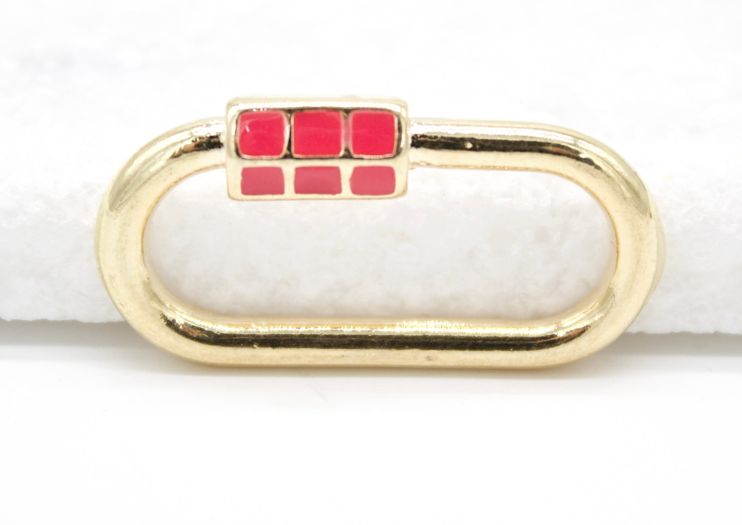 A polished gold oval charm features a vibrant red enameled clasp accenting its side.