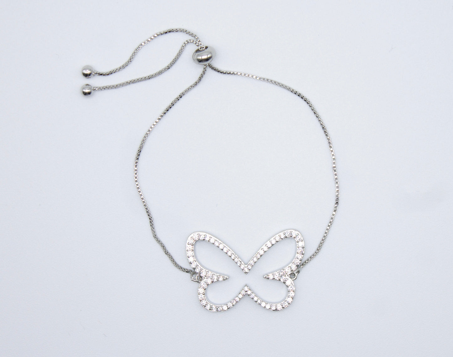 A silver adjustable bolo bracelet features a sparkling crystal-encrusted butterfly charm resting against a plain white background.
