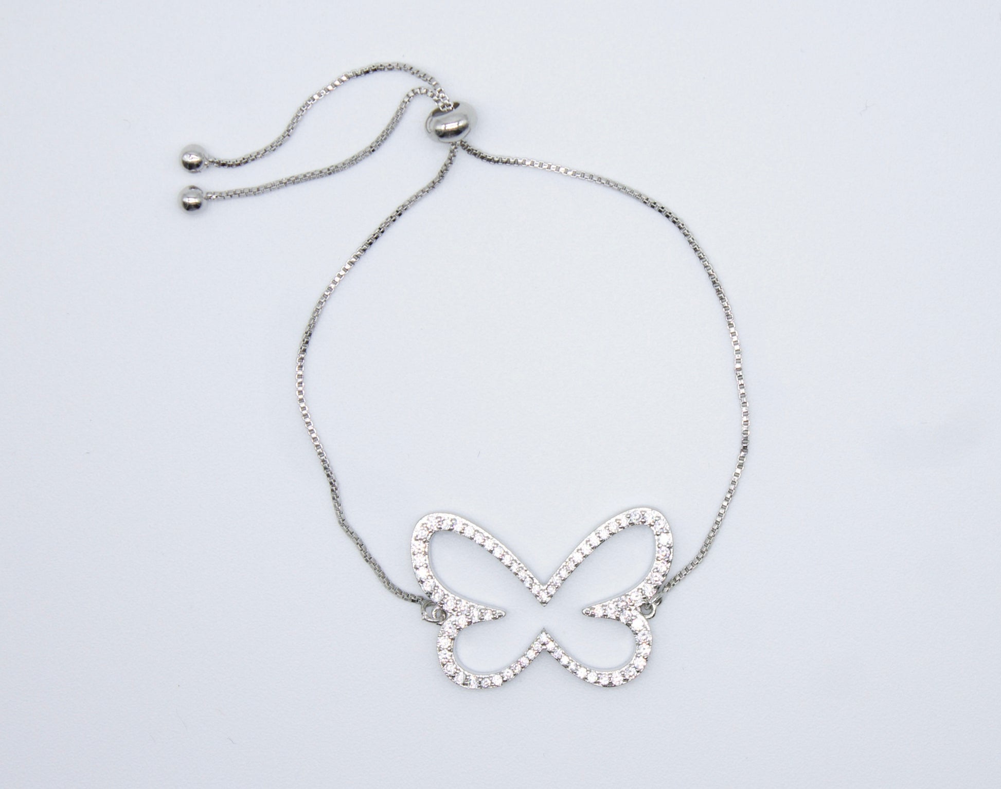 A silver adjustable bolo bracelet features a sparkling crystal-encrusted butterfly charm resting against a plain white background.