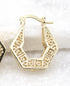 A gold hoop earring featuring an intricate geometric Greek key pattern rests against a light, textured surface.