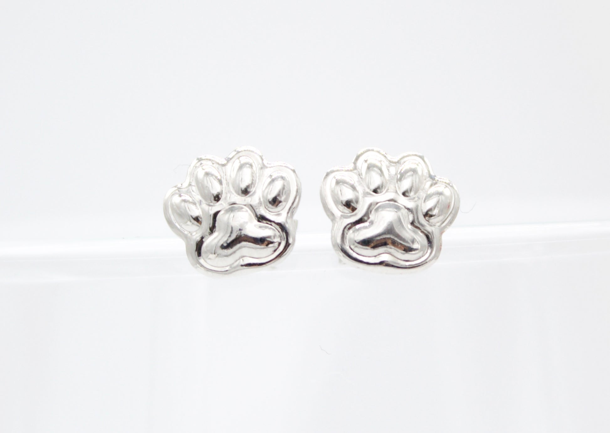 A pair of sterling silver paw print stud earrings rest against a clean white background.