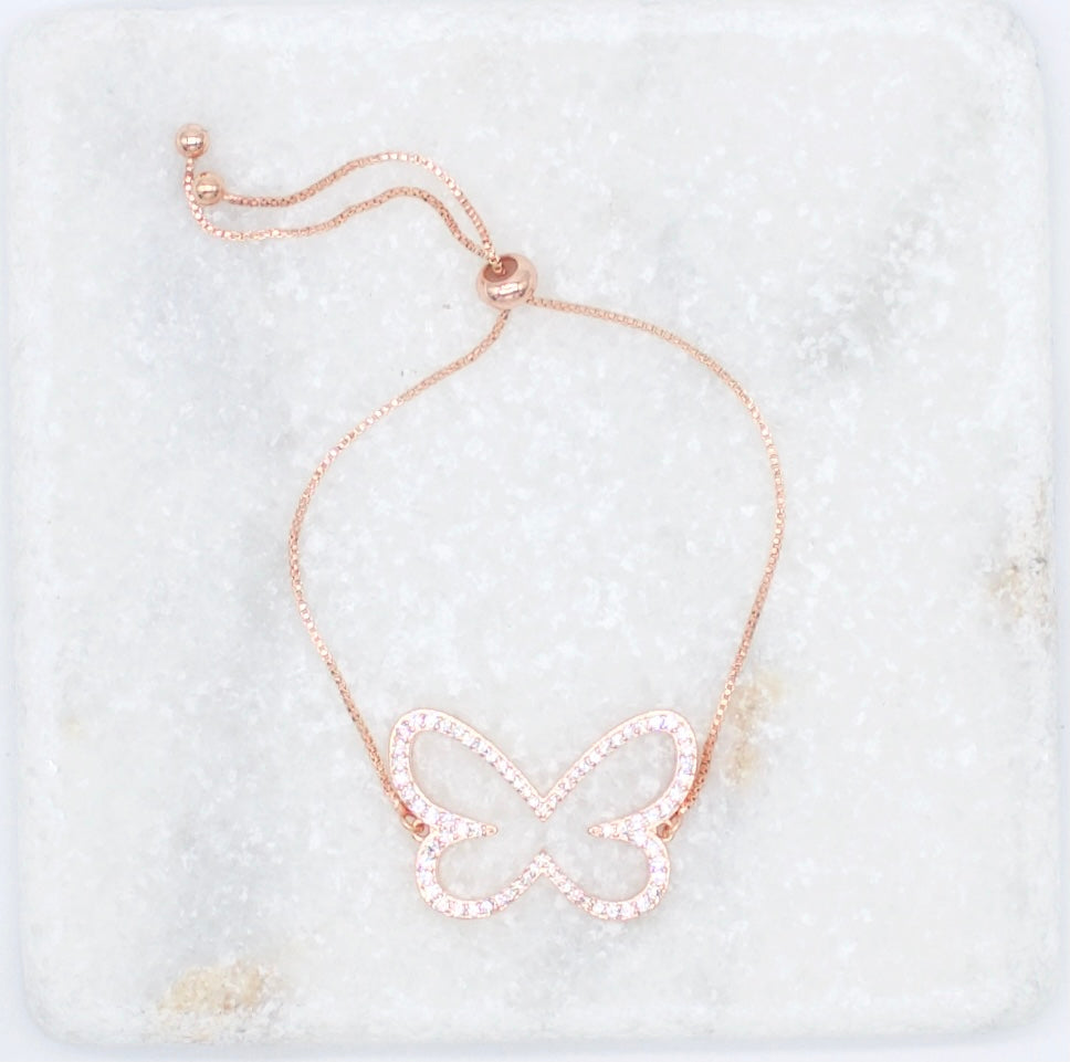 A rose gold butterfly slider bracelet adorned with sparkling cubic zirconia crystals rests on a light marble surface.