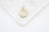 A gold evil eye charm pendant encrusted with sparkling cubic zirconia stones rests elegantly on a white marble surface.