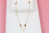 A delicate gold chain necklace with interspersed heart charms rests on a white display against a pink background.