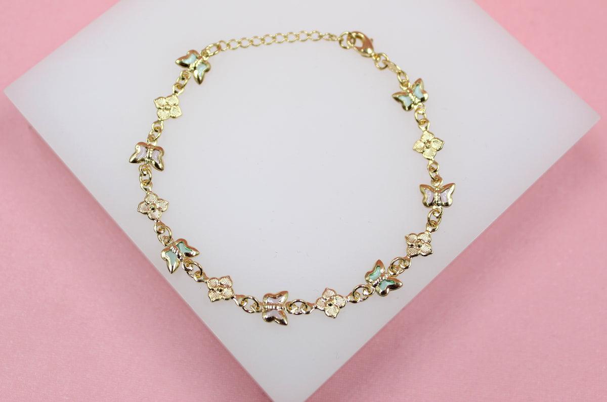 A delicate gold bracelet featuring alternating enameled butterfly charms and floral links rests on a white display surface against a pink background.