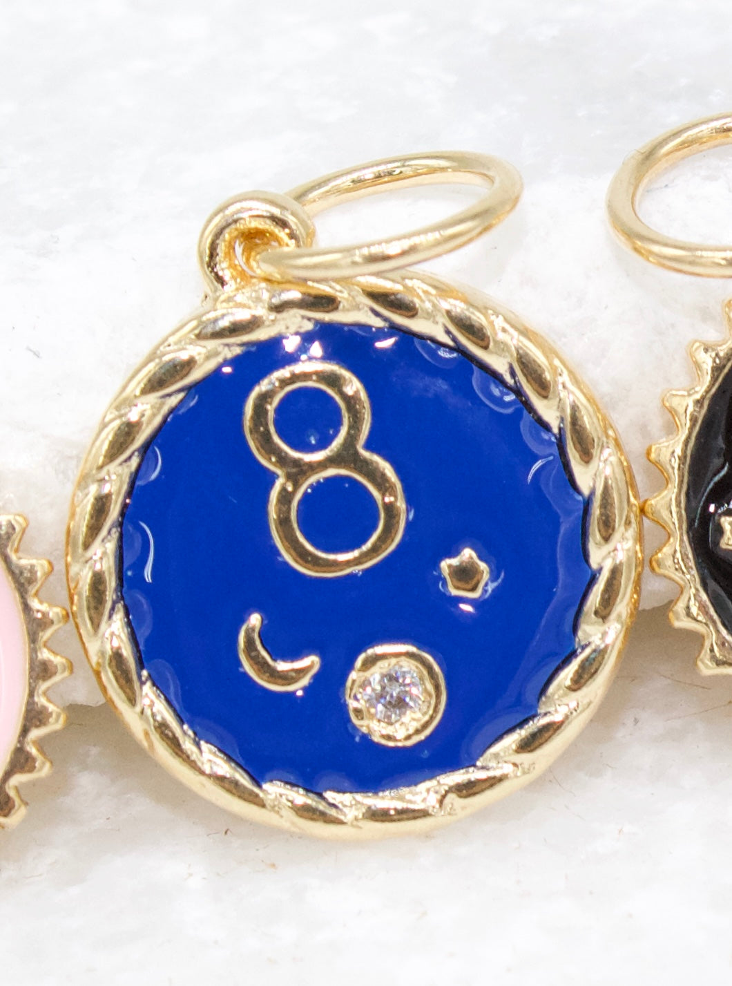 A round gold pendant features vibrant blue enamel with a gold number 8, crescent moon, and sparkling crystal accents.
