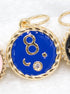 A round gold pendant features vibrant blue enamel with a gold number 8, crescent moon, and sparkling crystal accents.