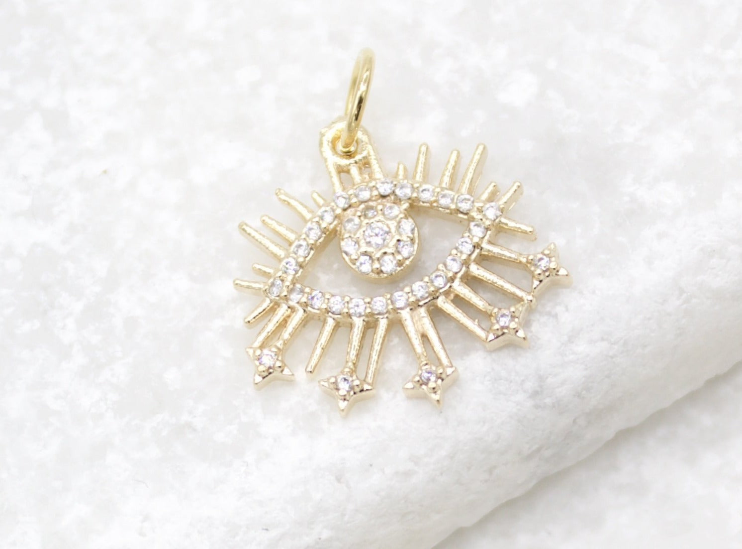 A sparkling gold evil eye pendant embellished with cubic zirconia crystals rests on a textured white surface.