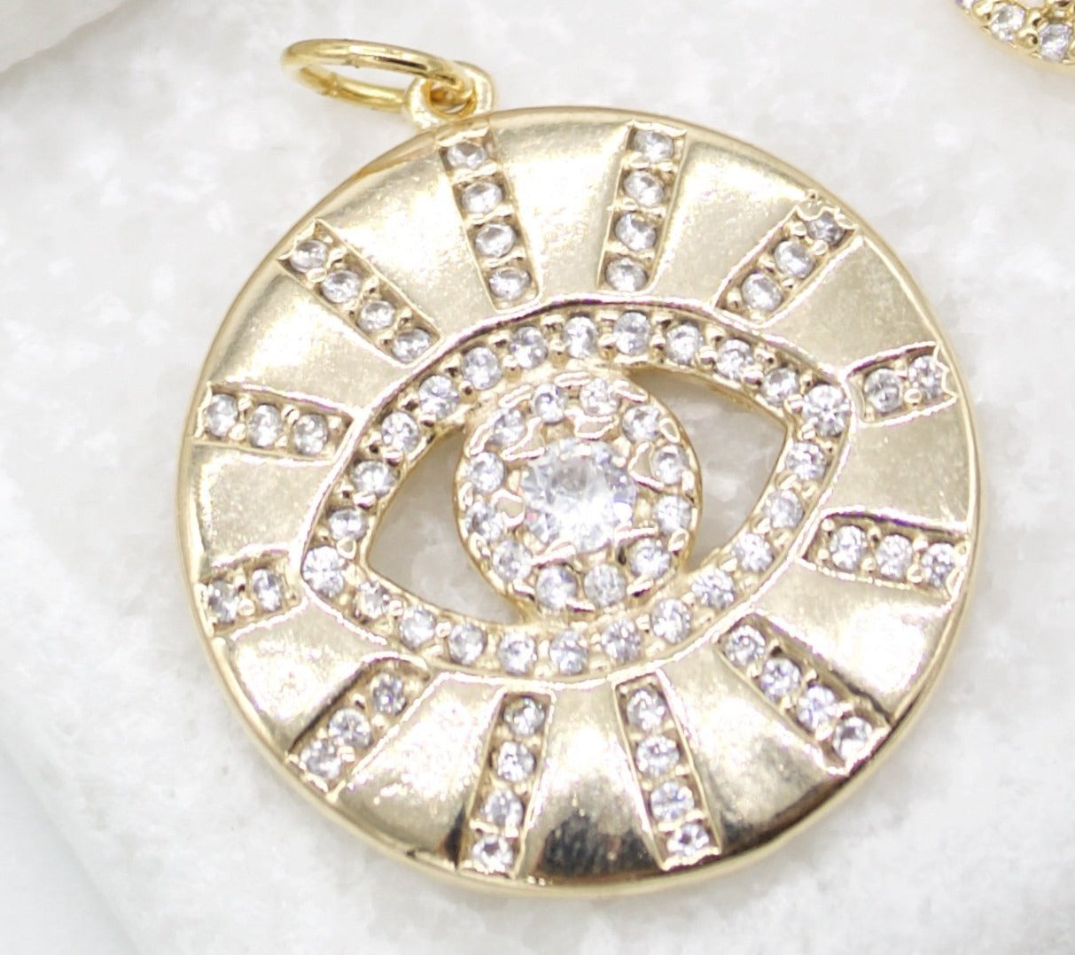 A gold evil eye pendant sparkles with pave-set cubic zirconia crystals arranged in a protective sunburst design.