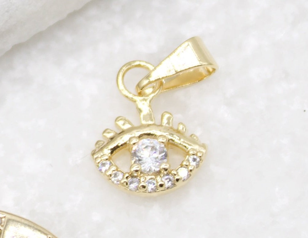 A gold evil eye charm featuring a sparkling cubic zirconia center rests on a white textured surface.