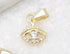 A gold evil eye charm featuring a sparkling cubic zirconia center rests on a white textured surface.