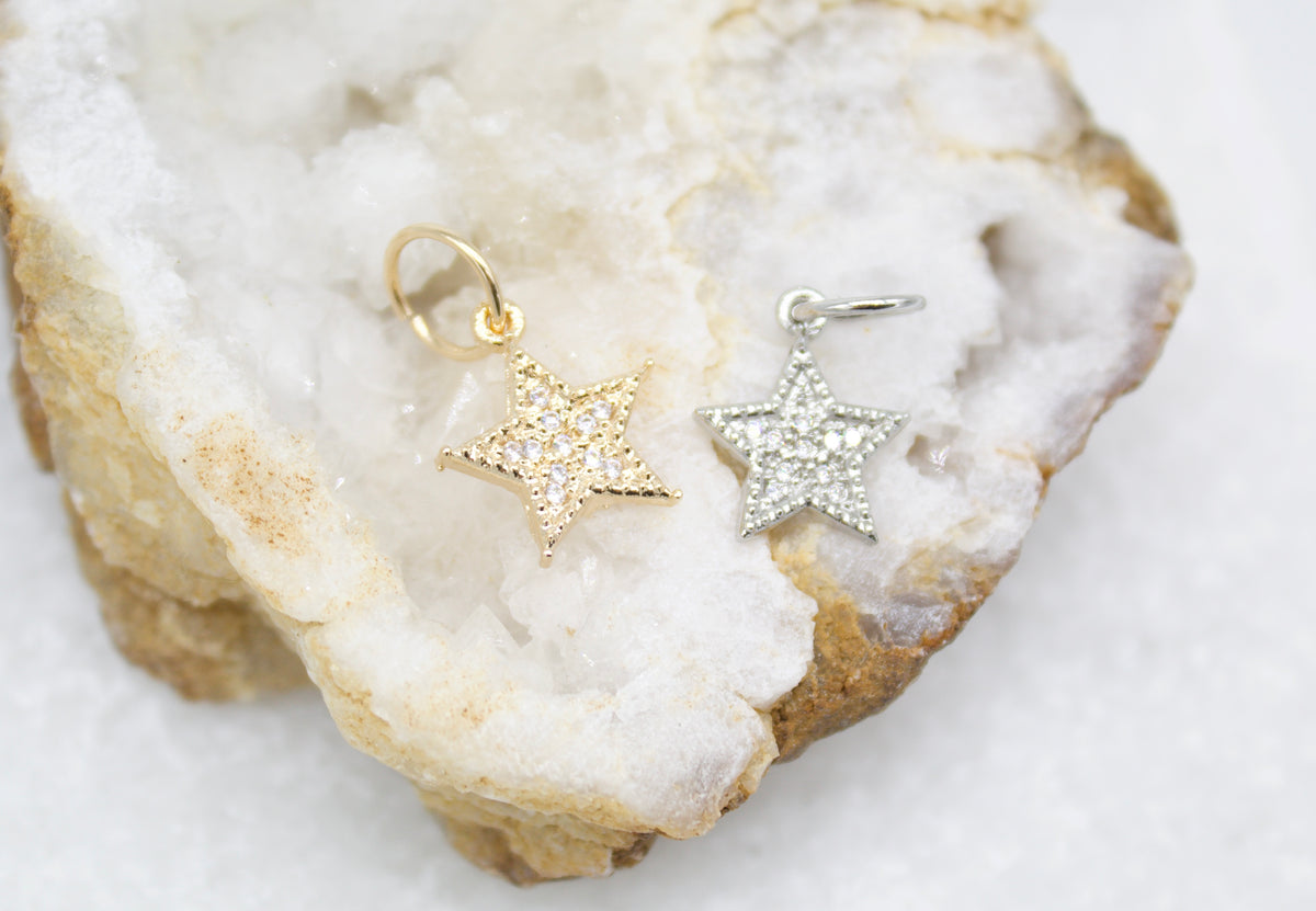 A gold and a silver star pendant embellished with sparkling pave crystals rest side by side on a textured white geode crystal.