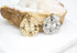 A gold compass rose pendant and a silver compass rose pendant rest side by side on a crystal geode.